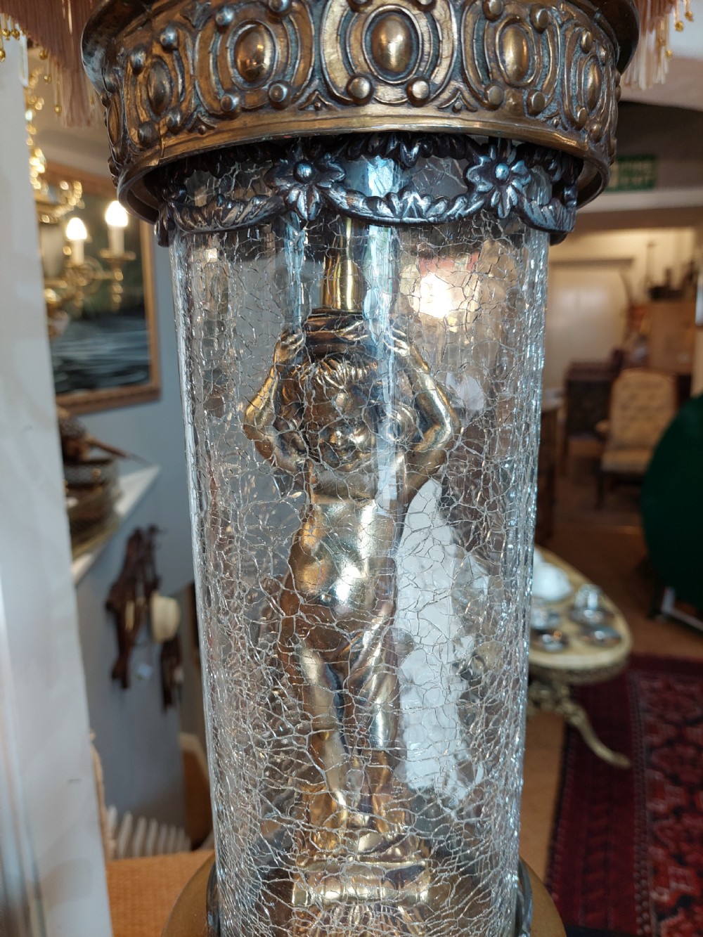 A pair of ornate gilded spelter table lamps featuring classical figures enclosed in glass columns topped with fringed cream fabric shades. View III