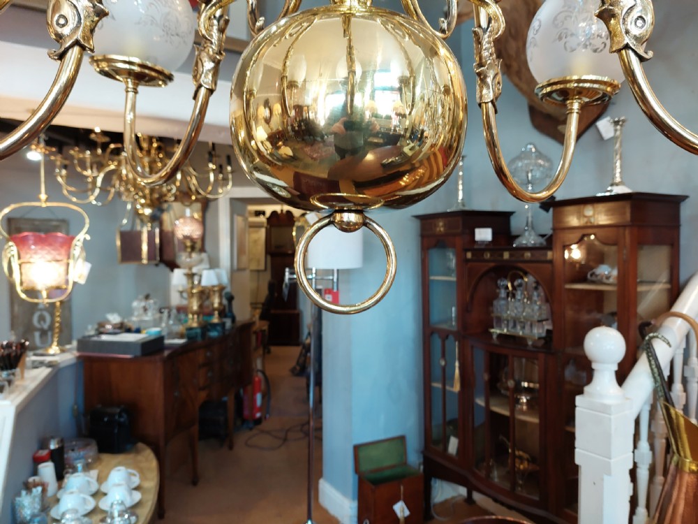 An early twentieth-century polished brass eight-arm chandelier featuring etched frosted glass shades mounted on curved arms around a central baluster stem. View V