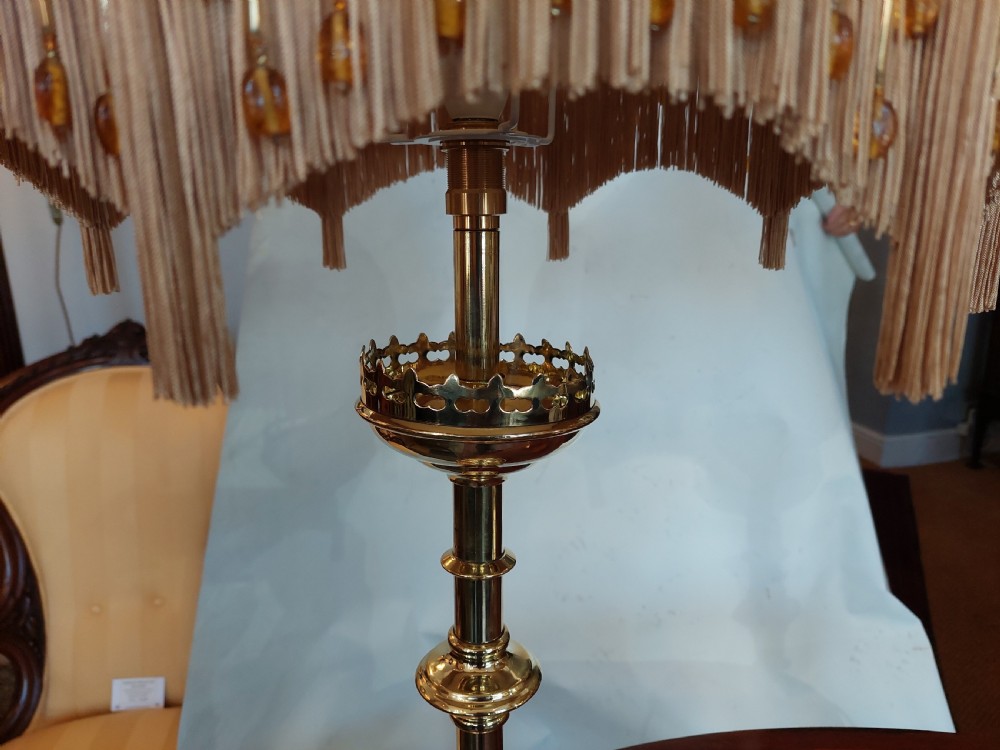 A pair of 19th-century Gothic Revival brass altar candlesticks converted into table lamps with patterned cream fabric shades featuring tassel fringe. View II