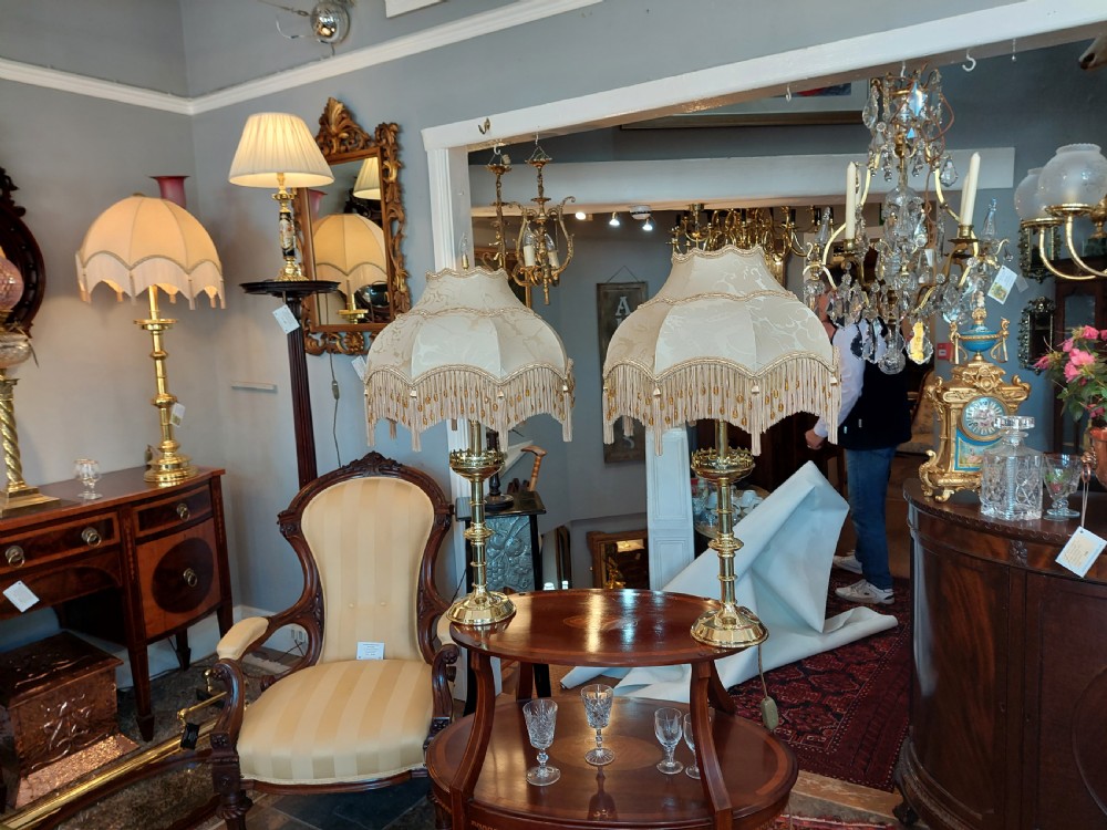 A pair of 19th-century Gothic Revival brass altar candlesticks converted into table lamps with patterned cream fabric shades featuring tassel fringe. View VI