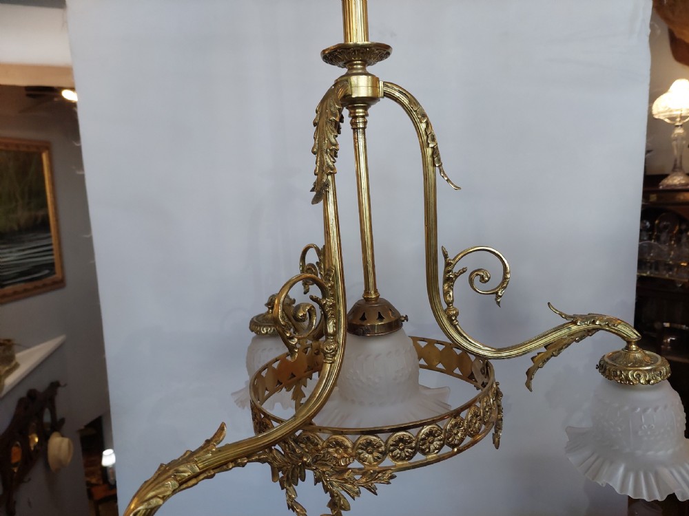 An early 20th-century French cast brass three-light chandelier featuring scrolled arms, a decorative pierced gallery ring, and frosted fluted glass shades. View III
