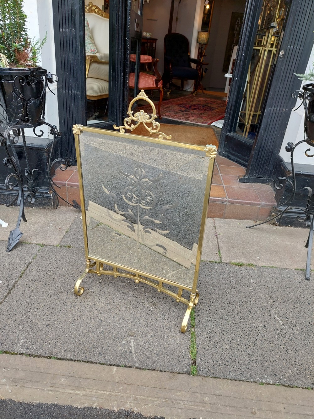 An Art Nouveau brass fire screen featuring a bevelled glass panel etched with a stylised floral motif, resting on splayed brass feet with a decorative top handle. View III