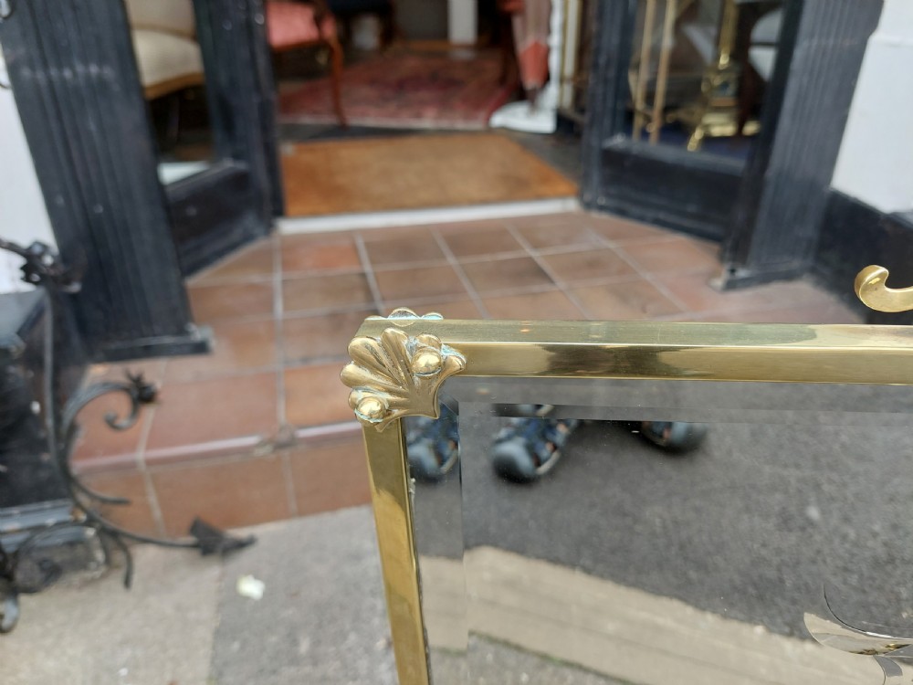 An Art Nouveau brass fire screen featuring a bevelled glass panel etched with a stylised floral motif, resting on splayed brass feet with a decorative top handle. View V