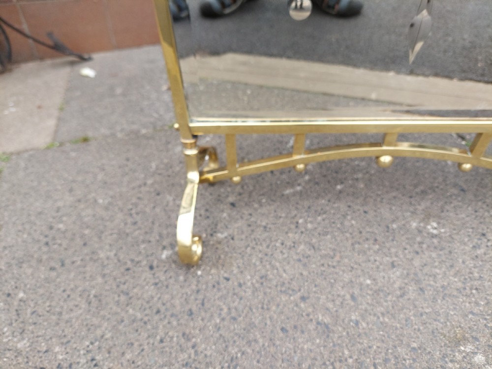 An Art Nouveau brass fire screen featuring a bevelled glass panel etched with a stylised floral motif, resting on splayed brass feet with a decorative top handle. View VI