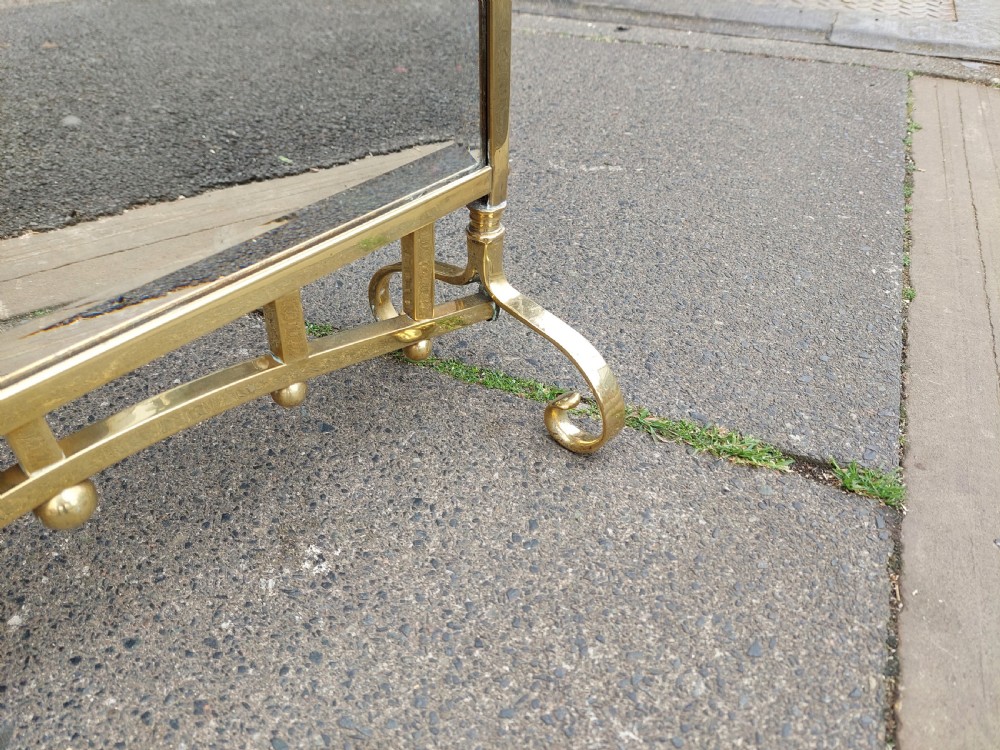 An Art Nouveau brass fire screen featuring a bevelled glass panel etched with a stylised floral motif, resting on splayed brass feet with a decorative top handle. View VII