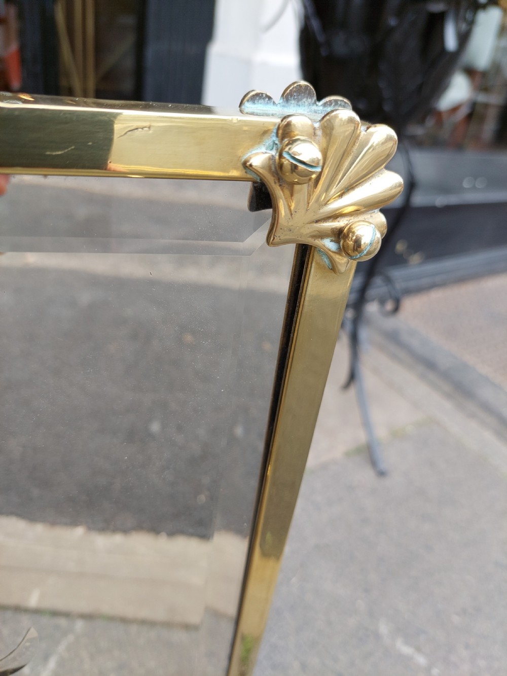 An Art Nouveau brass fire screen featuring a bevelled glass panel etched with a stylised floral motif, resting on splayed brass feet with a decorative top handle. View VIII