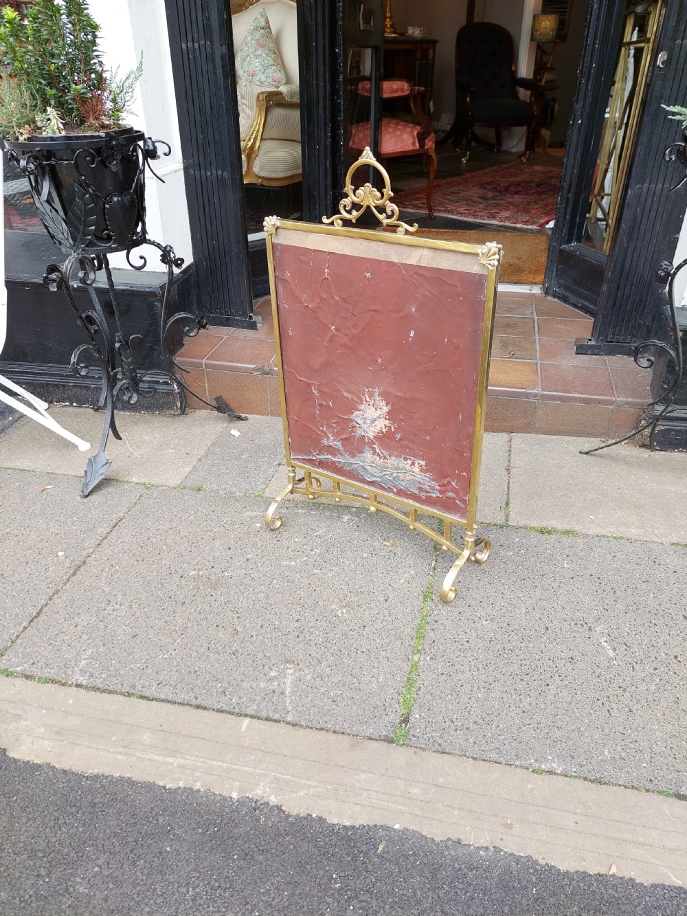An Art Nouveau brass fire screen featuring a bevelled glass panel etched with a stylised floral motif, resting on splayed brass feet with a decorative top handle. View IX