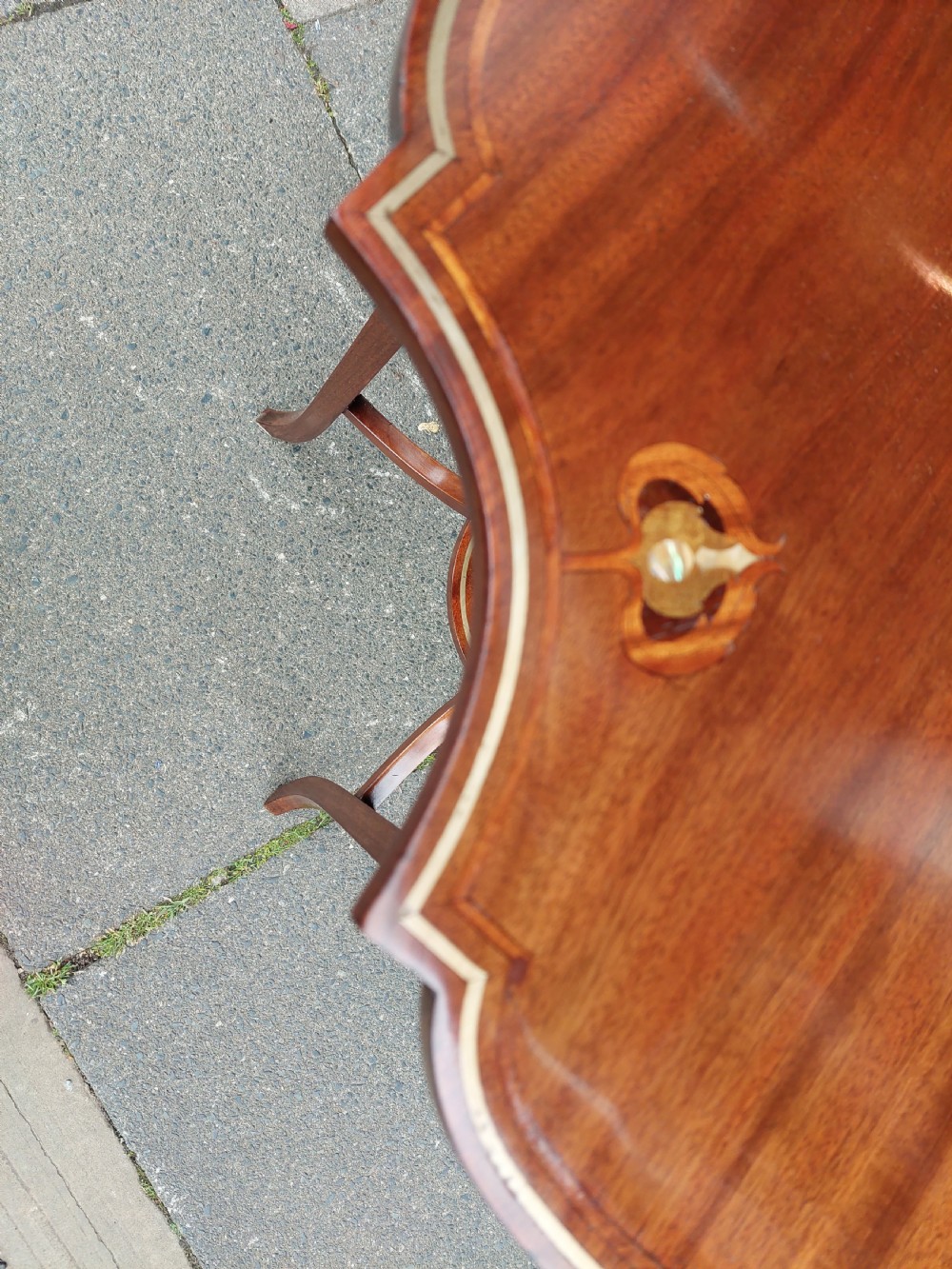 An Edwardian mahogany occasional table featuring a serpentine shaped top with inlaid floral motifs, slender splayed legs, and a central circular lower shelf. View VII