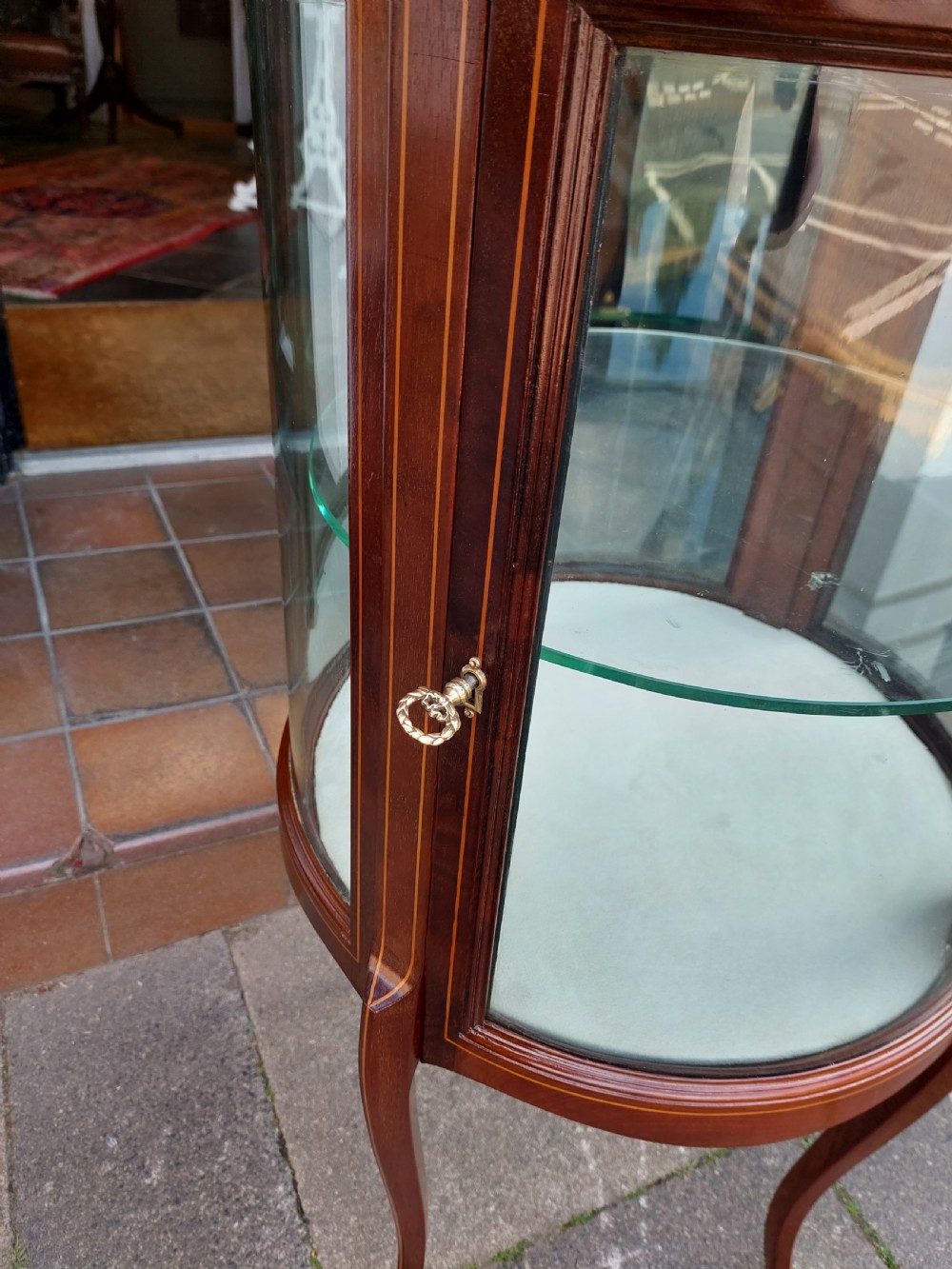 An Edwardian mahogany and marquetry oval bijouterie display table featuring curved glass sides, cabriole legs, and a glazed top. View IV