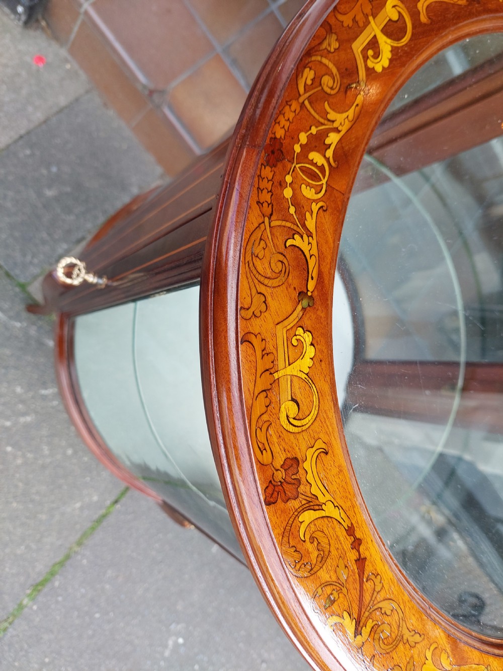 An Edwardian mahogany and marquetry oval bijouterie display table featuring curved glass sides, cabriole legs, and a glazed top. View V