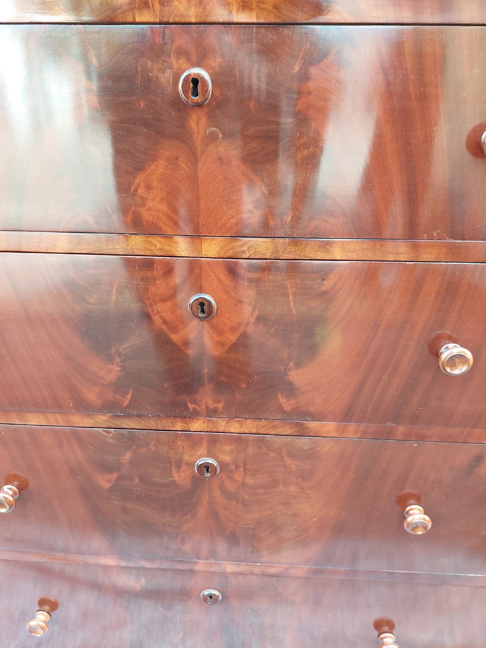 A tall Victorian flame mahogany semainier chest featuring seven stacked drawers with turned wooden handles set on a plinth base. View III