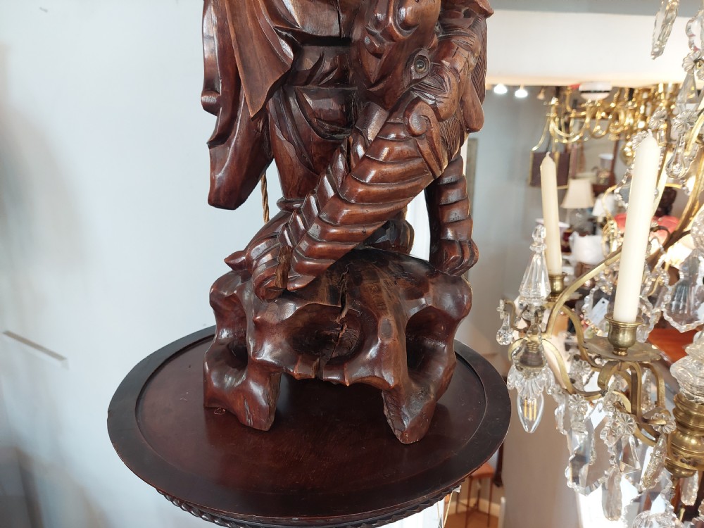 An early 20th-century Chinese carved rootwood table lamp featuring a figural base and a cylindrical shade with cream fringe and red trim. View V