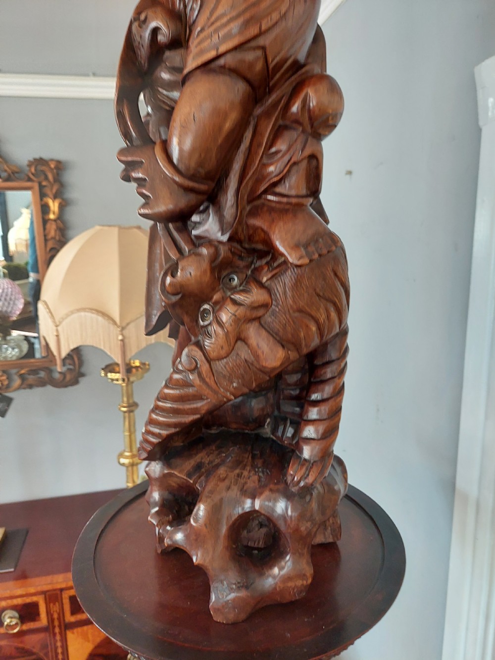 An early 20th-century Chinese carved rootwood table lamp featuring a figural base and a cylindrical shade with cream fringe and red trim. View VI