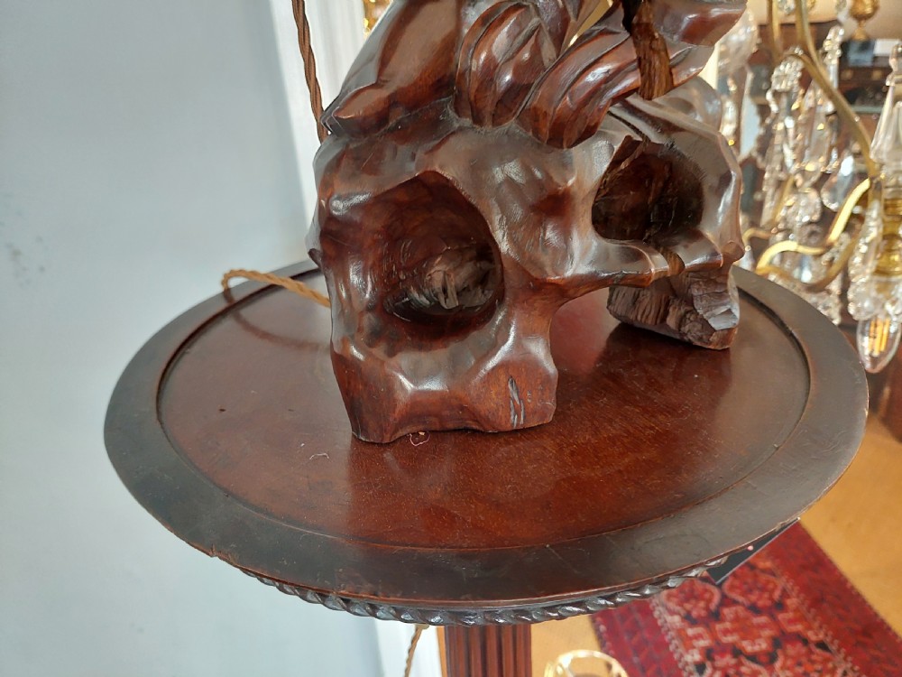 An early 20th-century Chinese carved rootwood table lamp featuring a figural base and a cylindrical shade with cream fringe and red trim. View X