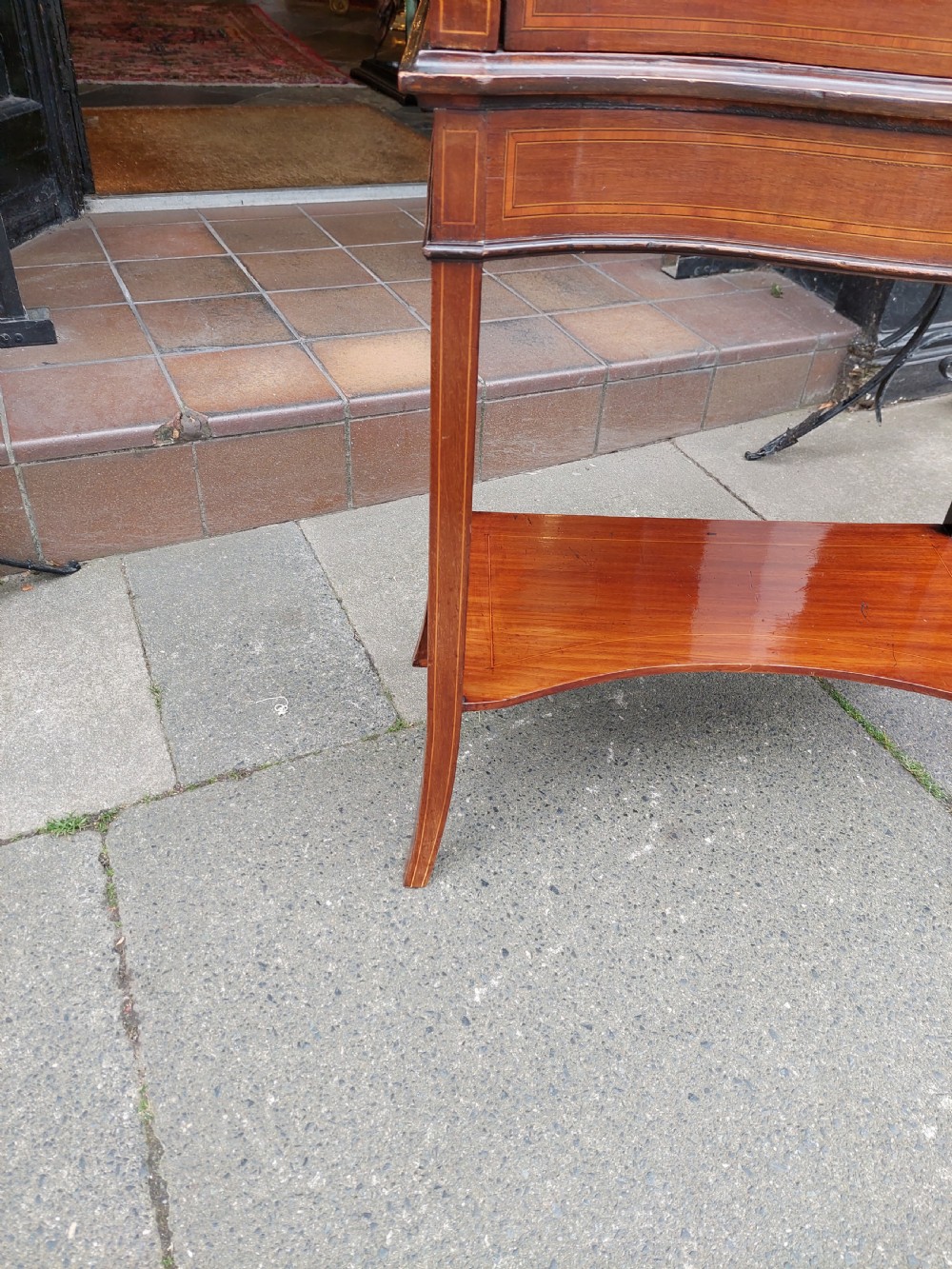 A late Victorian mahogany display cabinet featuring a serpentine glass door, satinwood stringing inlay, slender square tapered legs, and an lower undertier shelf. View II