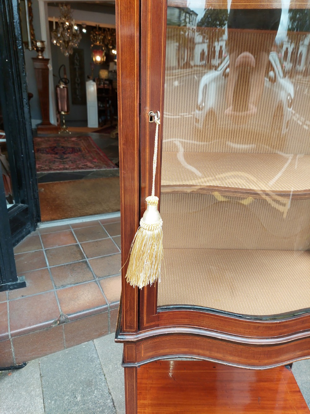 A late Victorian mahogany display cabinet featuring a serpentine glass door, satinwood stringing inlay, slender square tapered legs, and an lower undertier shelf. View III