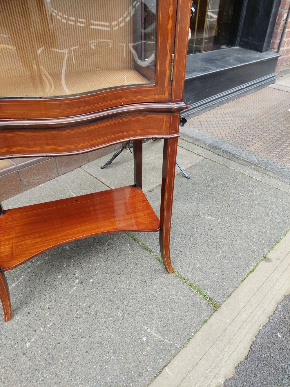 A late Victorian mahogany display cabinet featuring a serpentine glass door, satinwood stringing inlay, slender square tapered legs, and an lower undertier shelf. View IV