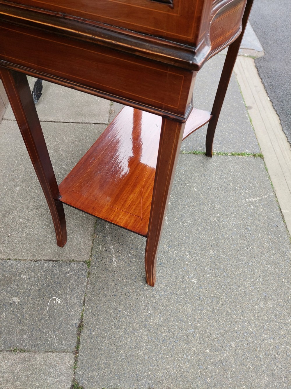 A late Victorian mahogany display cabinet featuring a serpentine glass door, satinwood stringing inlay, slender square tapered legs, and an lower undertier shelf. View V