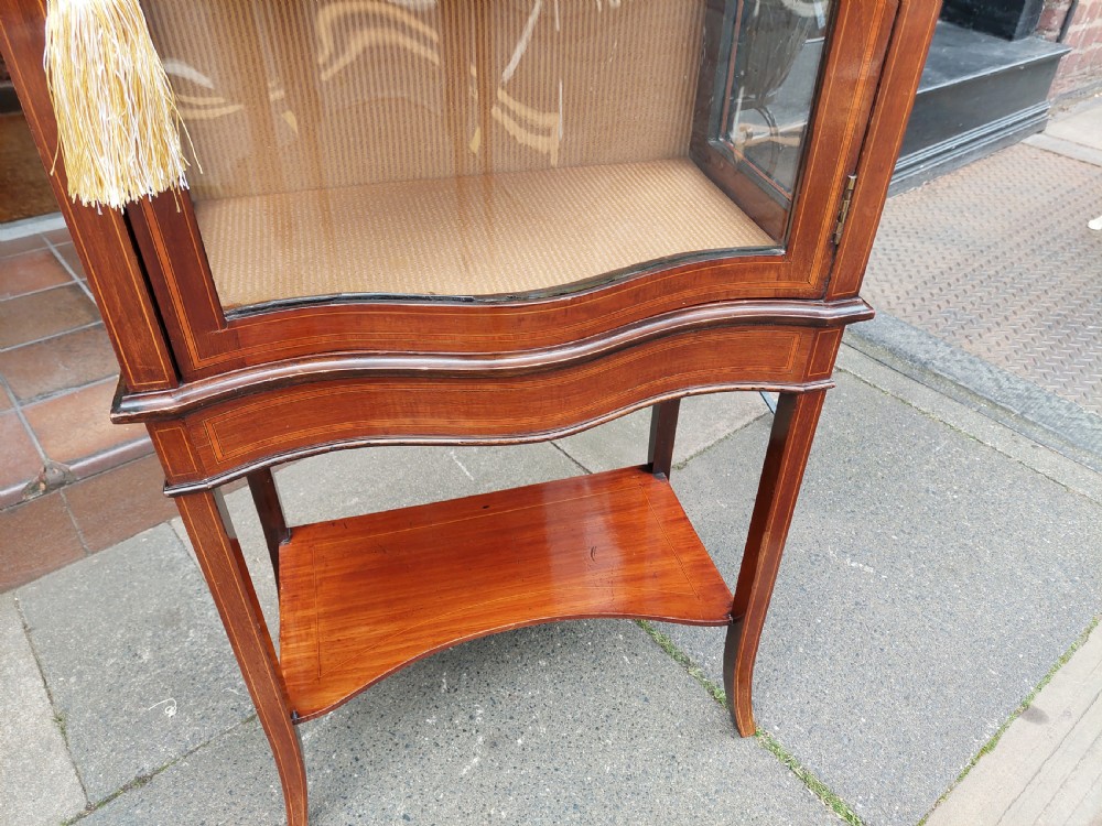 A late Victorian mahogany display cabinet featuring a serpentine glass door, satinwood stringing inlay, slender square tapered legs, and an lower undertier shelf. View VI
