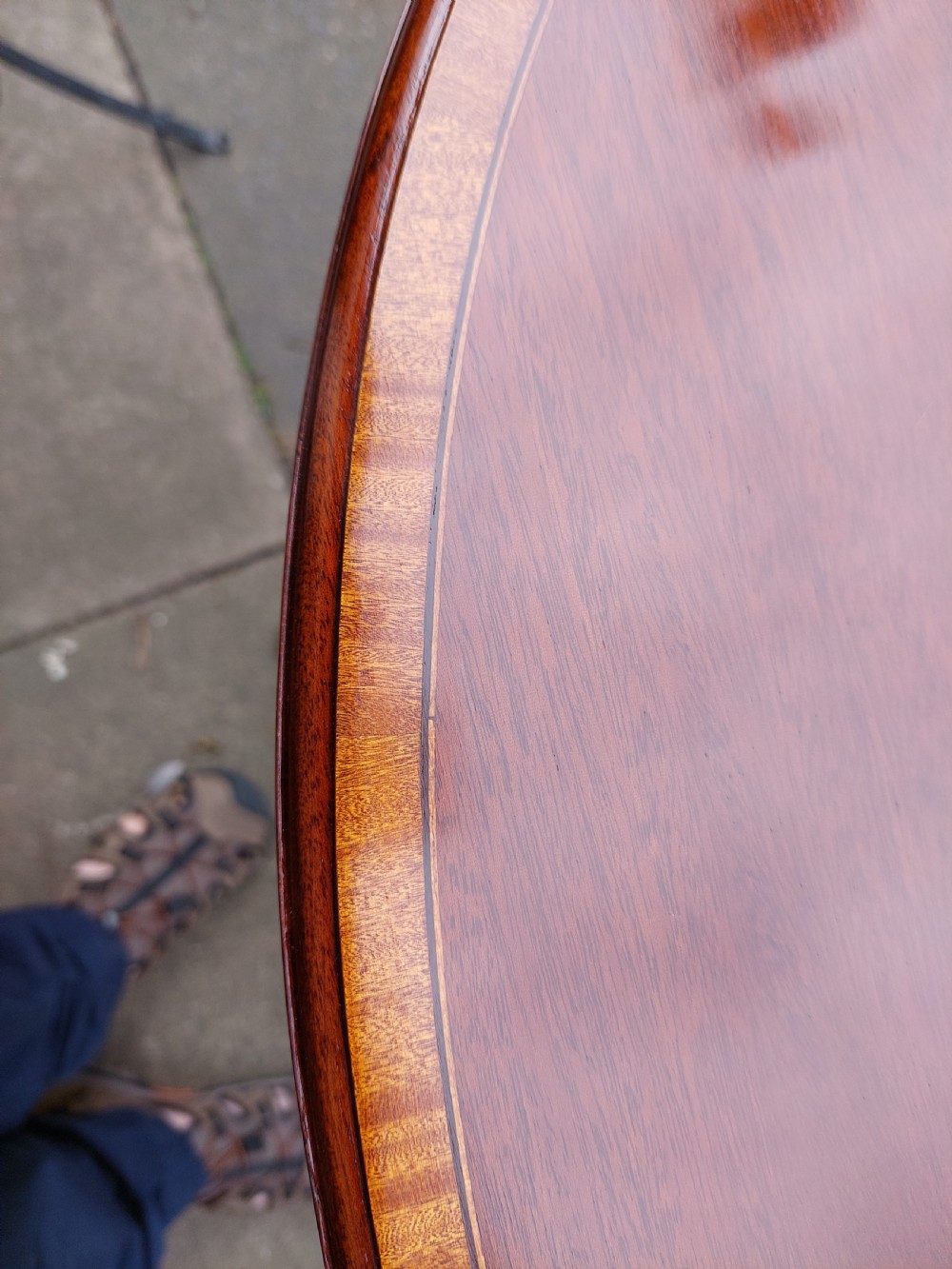 An oval Edwardian mahogany occasional table featuring satinwood crossbanding, a central inlaid motif, an oval undertier, and splayed tapered legs. View IV