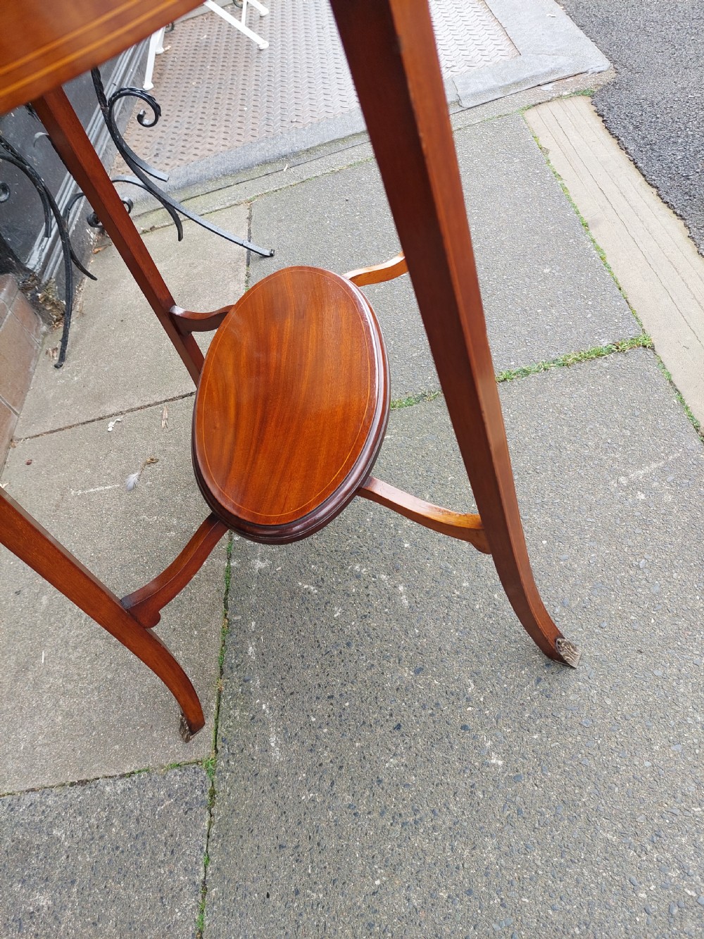 An oval Edwardian mahogany occasional table featuring satinwood crossbanding, a central inlaid motif, an oval undertier, and splayed tapered legs. View V