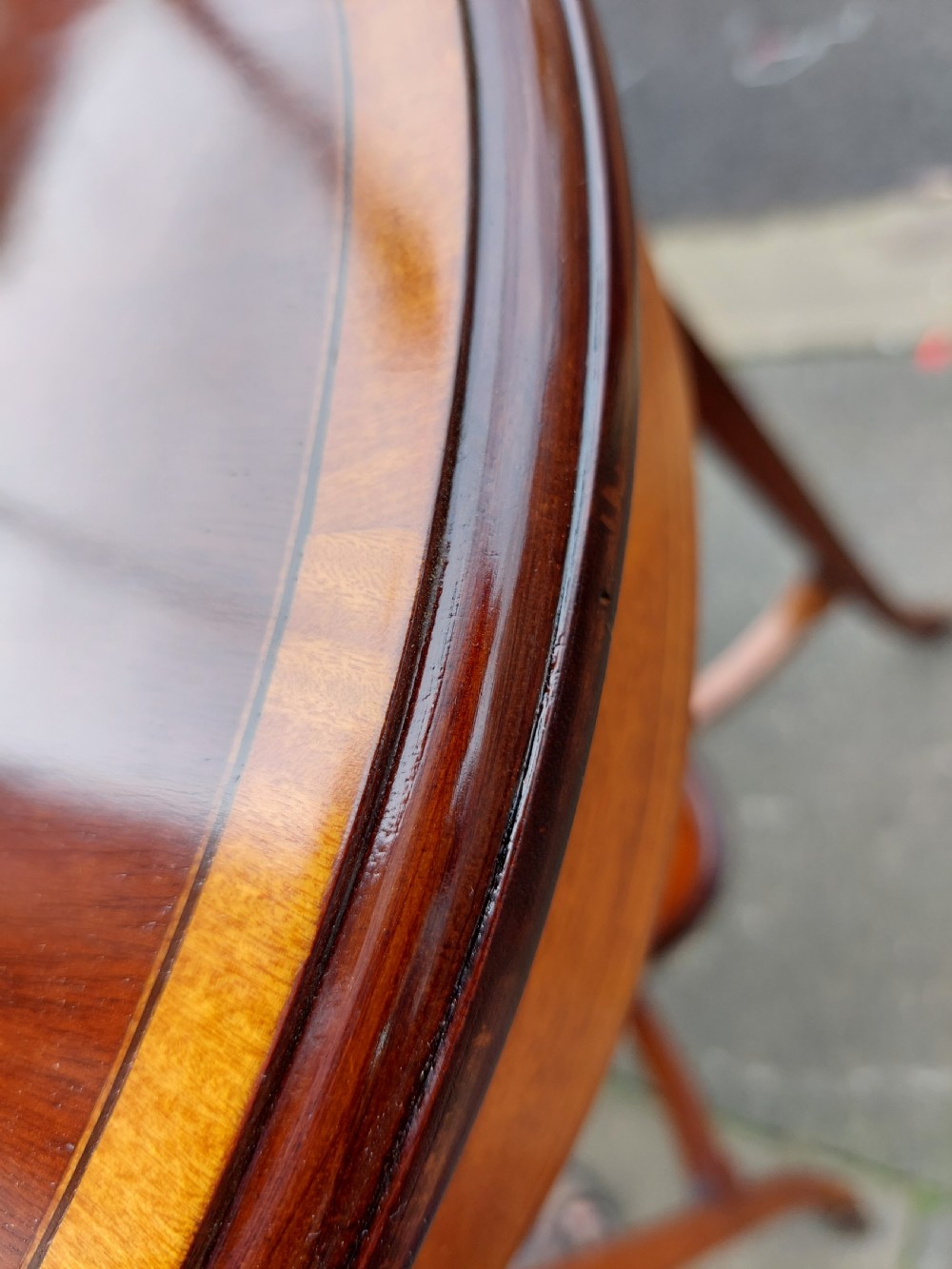 An oval Edwardian mahogany occasional table featuring satinwood crossbanding, a central inlaid motif, an oval undertier, and splayed tapered legs. View VI