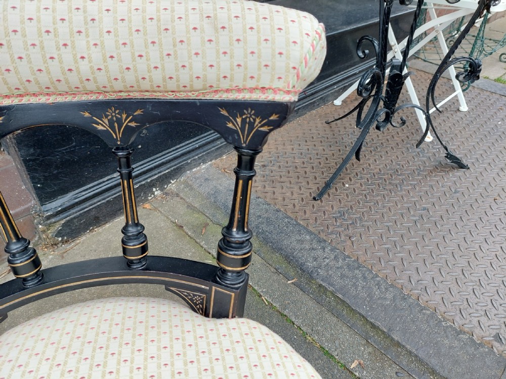 A pair of small Victorian ebonised chairs with cream patterned upholstery, turned spindles, gilt accents, and brass castors. View II