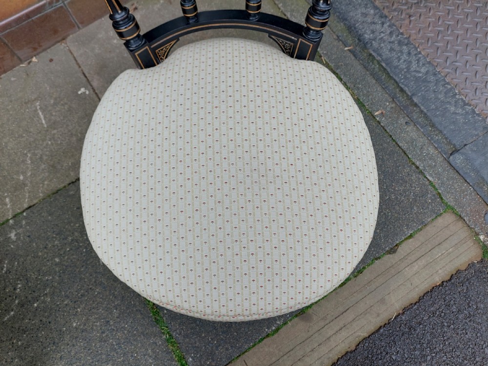 A pair of small Victorian ebonised chairs with cream patterned upholstery, turned spindles, gilt accents, and brass castors. View IV