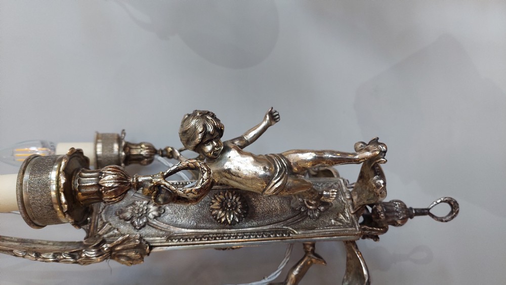 A mid-19th-century silver-plated ceiling light fitting decorated with sculpted cherub figures supporting candle sconces. View II