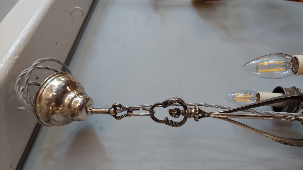 A mid-19th-century silver-plated ceiling light fitting decorated with sculpted cherub figures supporting candle sconces. View VI