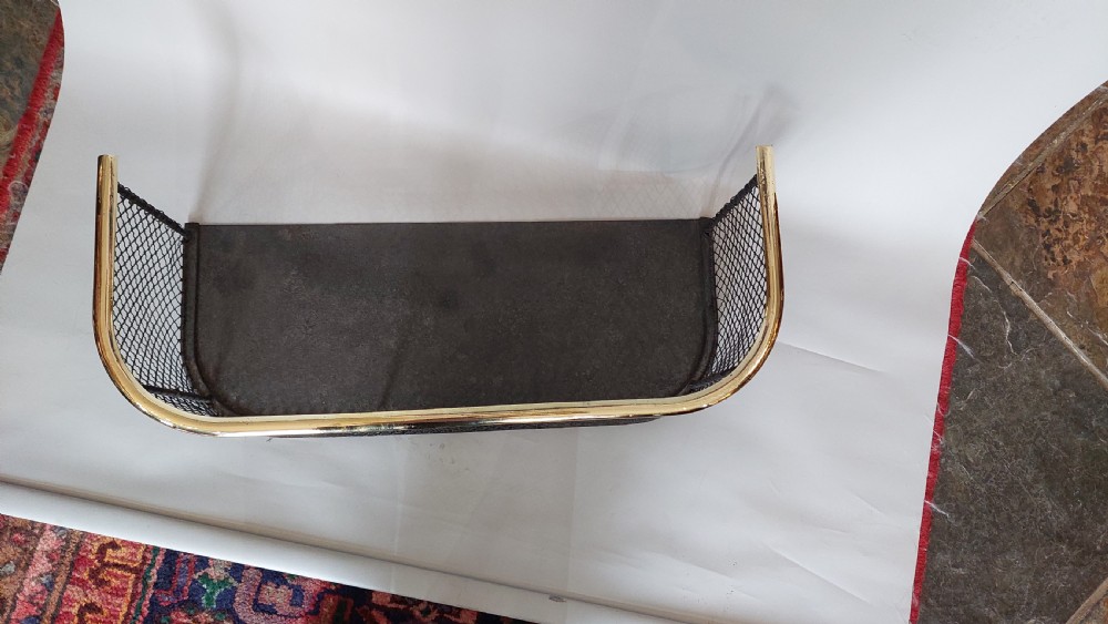 An early nineteenth-century U-shaped nursery fire guard with a polished brass top rail and a woven dark wire mesh body. View II