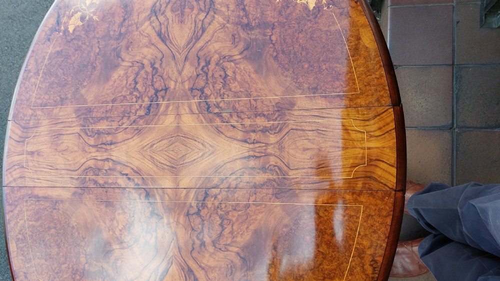 A Victorian burr walnut Sutherland table featuring floral marquetry inlay, twin turned column supports, and carved splayed legs fitted with ceramic castors. View X