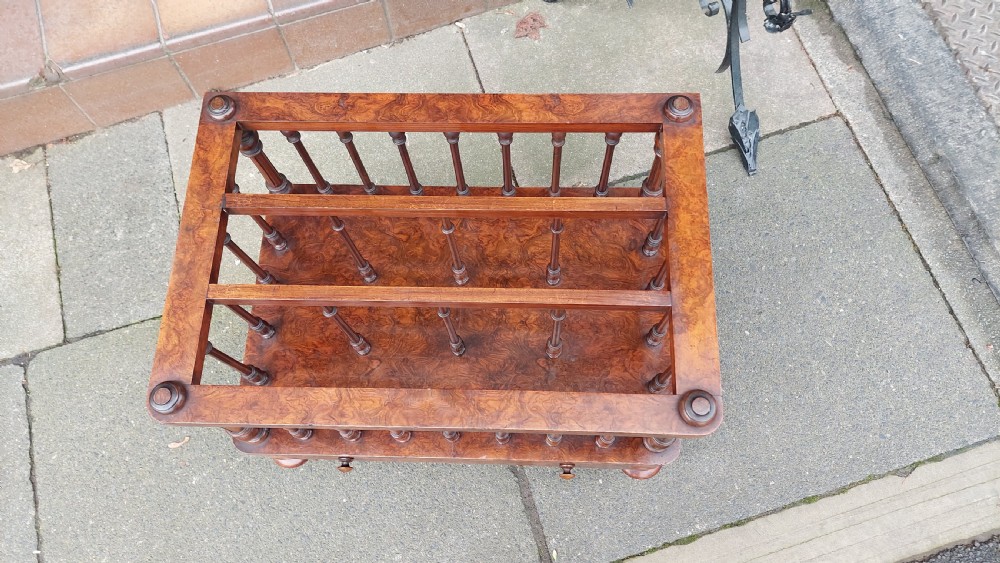 A Victorian walnut Canterbury featuring multiple open compartments formed by turned spindles, sitting above a single drawer with wooden knobs and turned legs on castors. View II