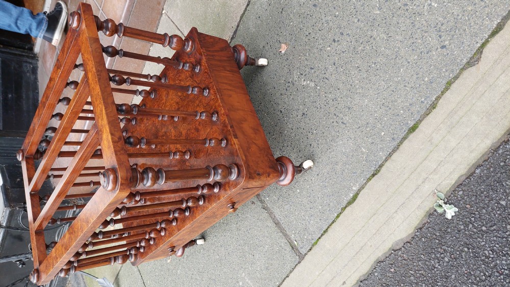 A Victorian walnut Canterbury featuring multiple open compartments formed by turned spindles, sitting above a single drawer with wooden knobs and turned legs on castors. View III