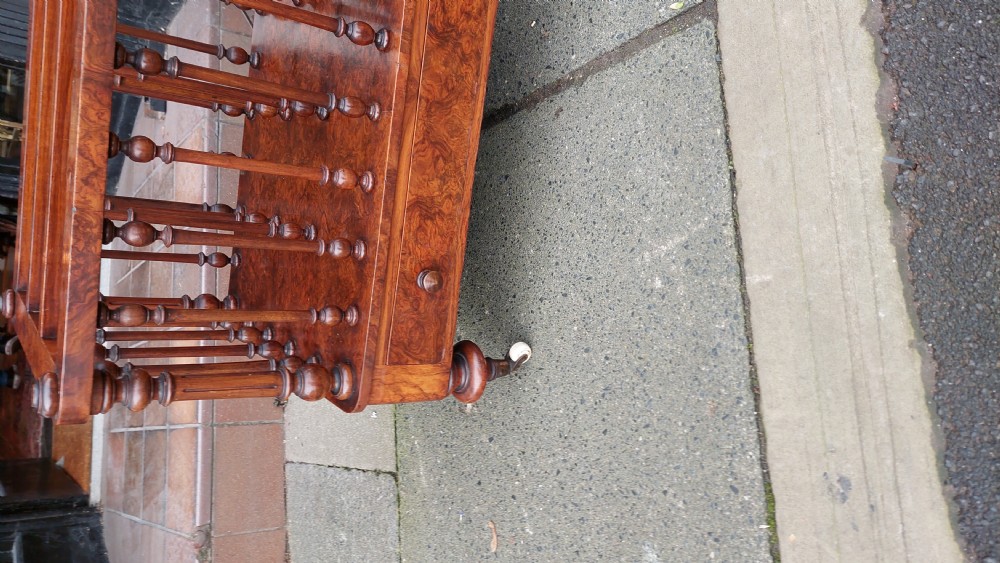 A Victorian walnut Canterbury featuring multiple open compartments formed by turned spindles, sitting above a single drawer with wooden knobs and turned legs on castors. View IV