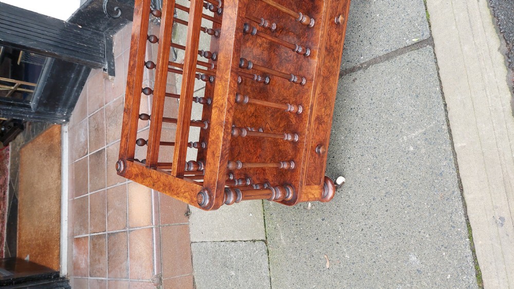 A Victorian walnut Canterbury featuring multiple open compartments formed by turned spindles, sitting above a single drawer with wooden knobs and turned legs on castors. View V