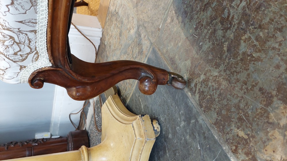 A Victorian low-seated nursing chair crafted from carved walnut featuring floral patterned cream fabric, spoon back, cabriole legs, and castors. View II