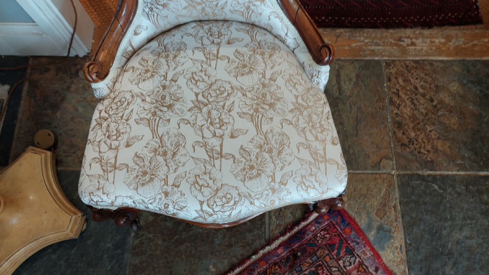 A Victorian low-seated nursing chair crafted from carved walnut featuring floral patterned cream fabric, spoon back, cabriole legs, and castors. View IV