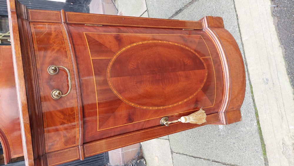 An Edwardian mahogany bedside cabinet featuring a curved front, single upper drawer, inlaid oval panel door, and shaped gallery top. View IV