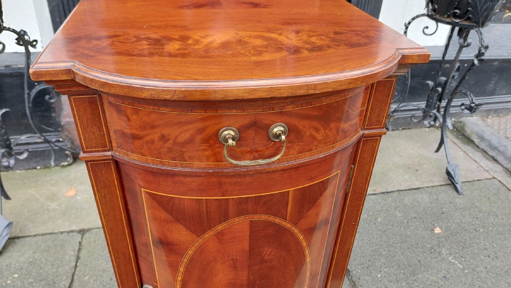 An Edwardian mahogany bedside cabinet featuring a curved front, single upper drawer, inlaid oval panel door, and shaped gallery top. View V