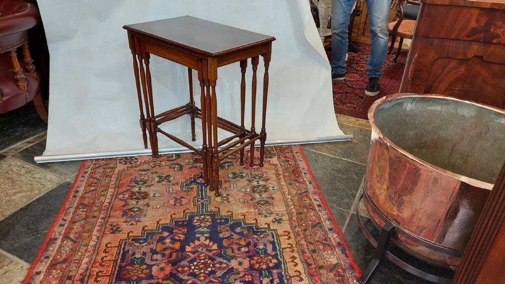 A set of three graduated Edwardian mahogany nesting tables featuring slender turned legs, cross-stretchers, and inset glass tops. View VI
