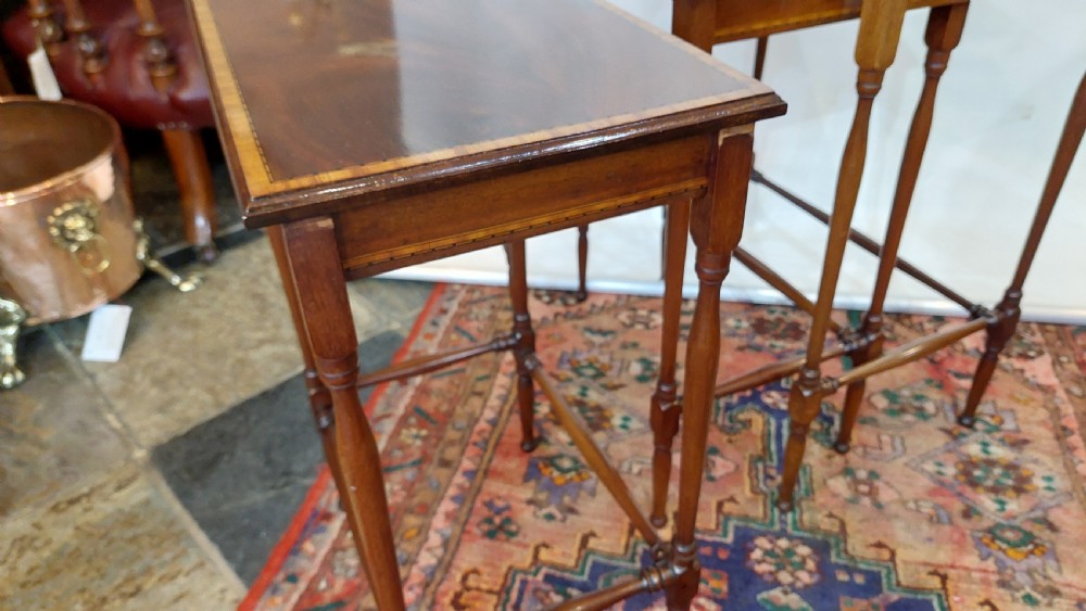 A set of three graduated Edwardian mahogany nesting tables featuring slender turned legs, cross-stretchers, and inset glass tops. View X
