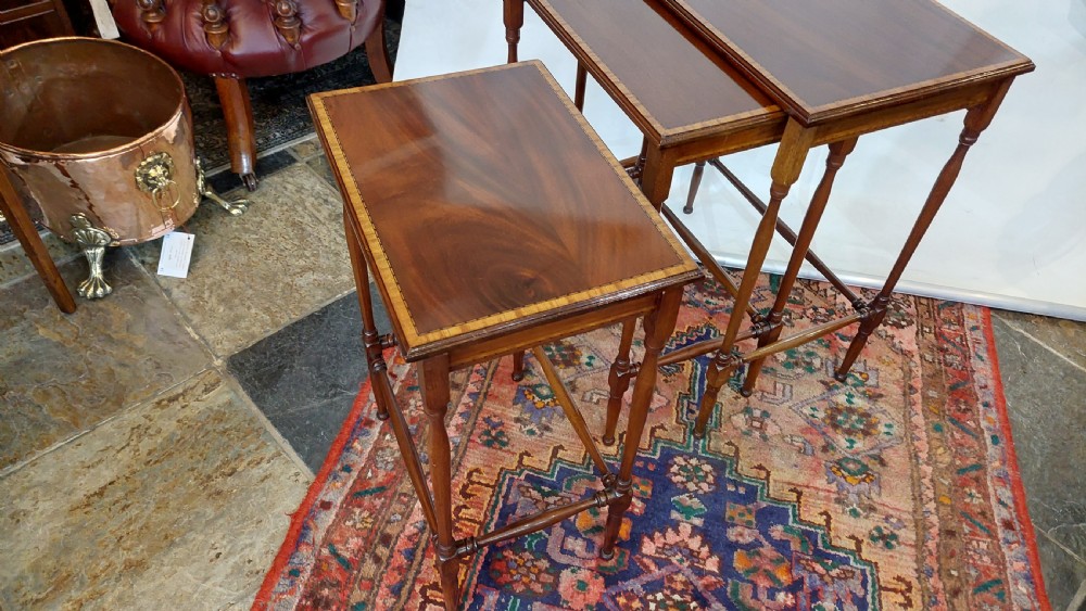 A set of three graduated Edwardian mahogany nesting tables featuring slender turned legs, cross-stretchers, and inset glass tops. View XI