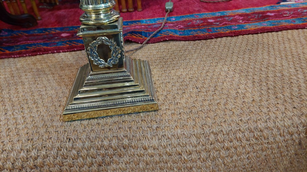 An early 20th-century brass table lamp featuring a fluted Corinthian column base on a stepped pedestal, topped with a cream domed shade trimmed with fringe and tassels. View II