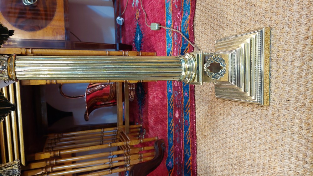 An early 20th-century brass table lamp featuring a fluted Corinthian column base on a stepped pedestal, topped with a cream domed shade trimmed with fringe and tassels. View III