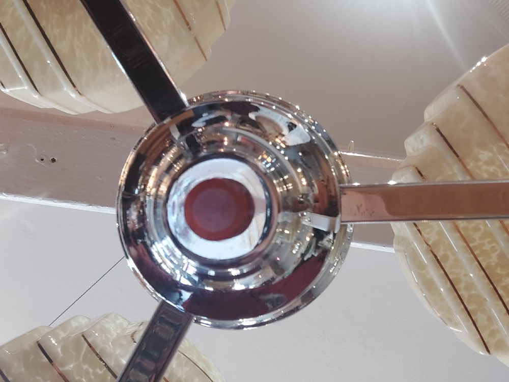 A three-arm Art Deco ceiling light fixture featuring chrome metalwork, reddish bakelite collars, and three mottled cream and amber glass bowl shades. View VI
