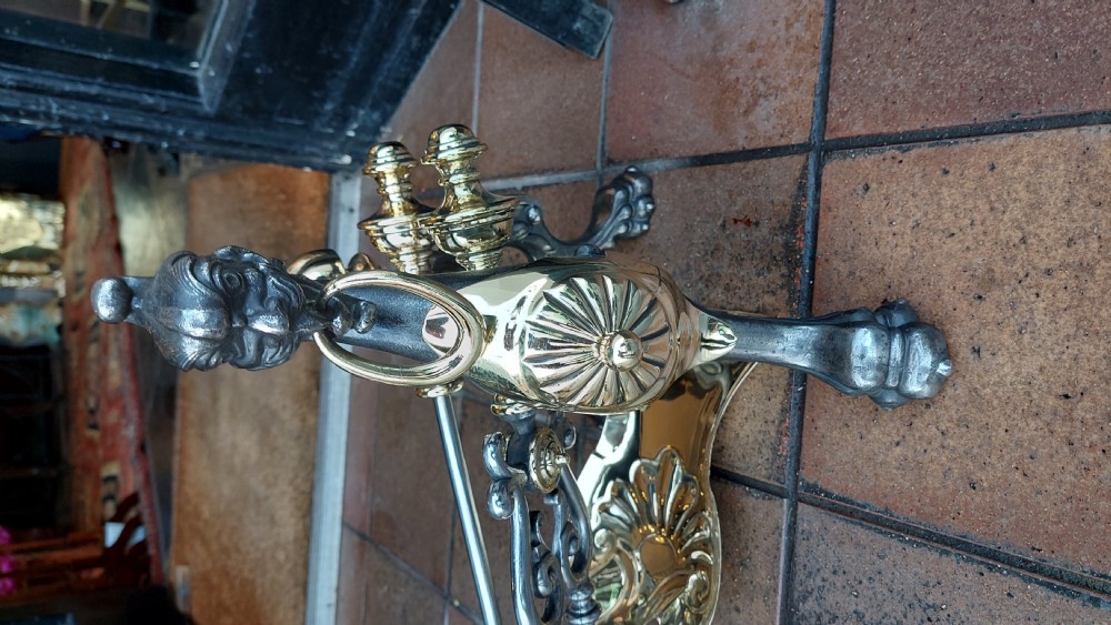 A set of Victorian hearth accessories comprising three metal fire tools resting across a pair of cast iron and brass decorated andirons. View II