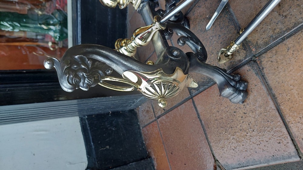 A set of Victorian hearth accessories comprising three metal fire tools resting across a pair of cast iron and brass decorated andirons. View III
