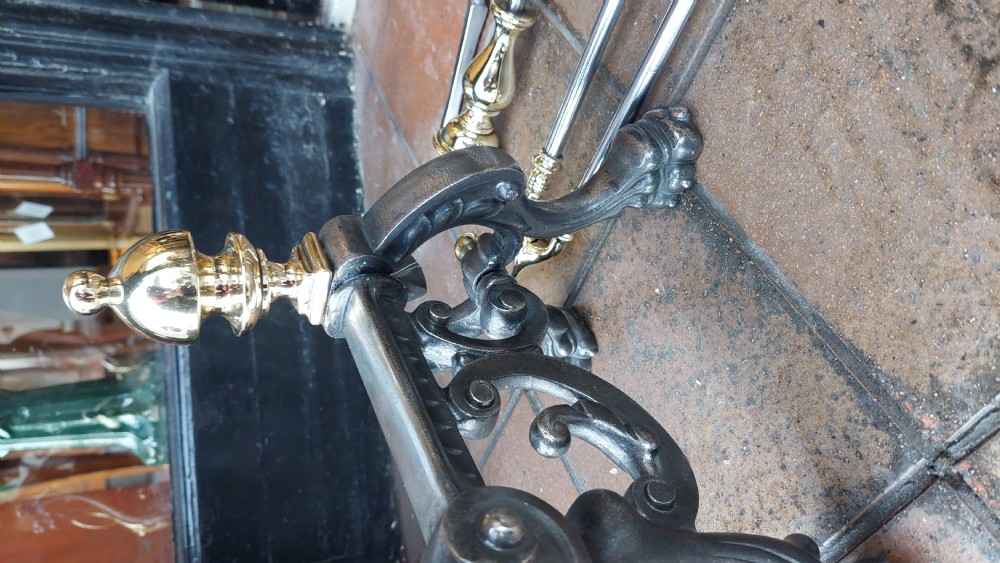 A set of Victorian hearth accessories comprising three metal fire tools resting across a pair of cast iron and brass decorated andirons. View V