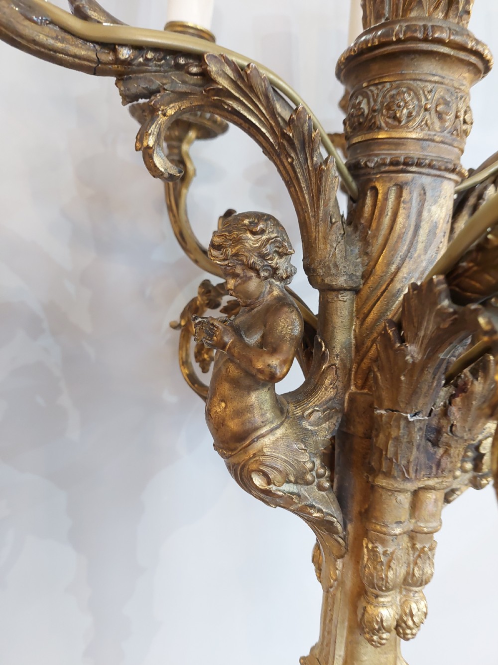 An early 20th-century six-arm gilt metal chandelier featuring carved cherub figures, scrolling acanthus leaf branches, and white candle sleeves. View II